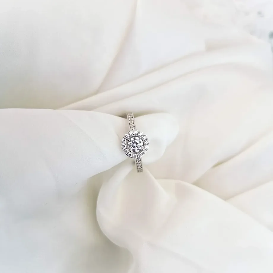 Anillo de compromiso halo: diamante central rodeado de diamantes pequeños, en oro blanco de 18 quilates, sobre seda color crudo